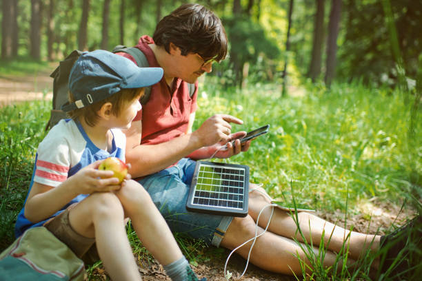 der kleine junge und sein vater verwenden tragbare solarbatterien, um smartphones in der natur aufzuladen. nachhaltiger lebensstil, ökologische alternative energien und ökologische konzepte. - energy fuel and power generation futuristic solar energy stock-fotos und bilder