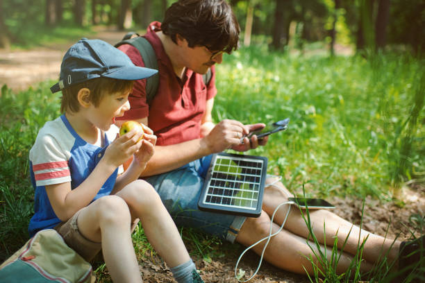 der kleine junge und sein vater verwenden tragbare solarbatterien, um smartphones in der natur aufzuladen. nachhaltiger lebensstil, ökologische alternative energien und ökologische konzepte. - energy fuel and power generation futuristic solar energy stock-fotos und bilder