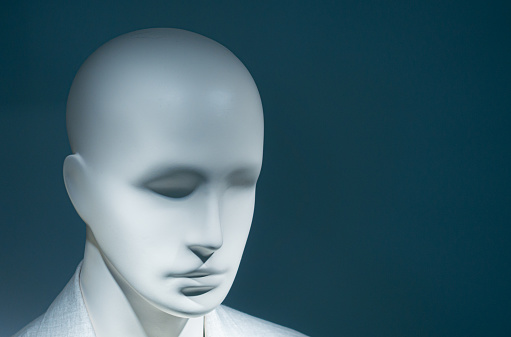 The face of a male mannequin in sunglasses behind the glass of a display case.