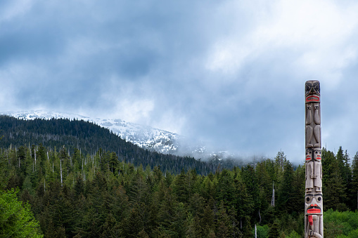 Ketchikan, Alaska, USA -May 21, 2022: Hand carved Totem pole and snowy ridge at Ketchikan Heritage Totem Pole Center