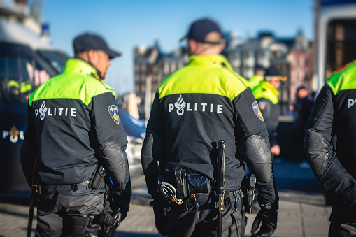 Dutch police squad formation and horseback riding mounted police back view with Police logo emblem on uniform maintain public order after football game and rally in the streets of Amsterdam