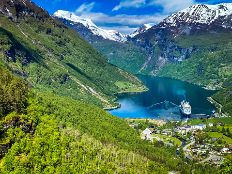 Geirangerfjord, Iceland-May 30, 2023-A luxury cruise ship is docked far below at the end of Geiranger Fjord for a brief visit to allow its passengers to enjoy this magnificent scenery for a few hours.