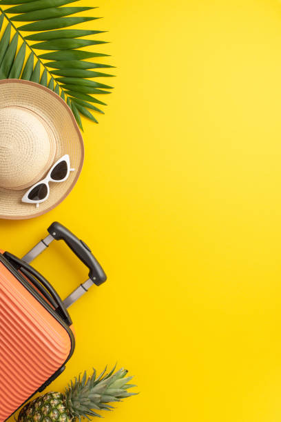 istock Craving blissful vacation. Top view vertical arrangement with suitcase, beach necessities, sunglasses, sunhat, palm leaf, juicy pineapple on vivid yellow background. Plenty of space for text or ads 1500376527