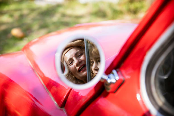 Happy senior woman driver in straw hat driving sitting in new car, smiling looking at camera enjoying journey. Driving courses and life insurance. Retired people activity and road trip concept