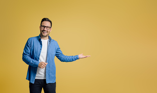 Portrait of happy salesman showing something on palm while standing against yellow background