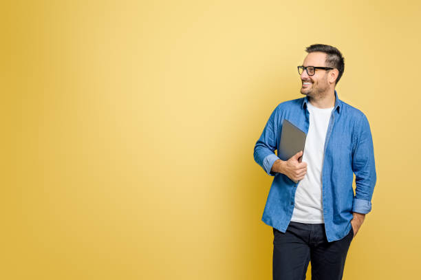 счастливый мужчина-фрилансер с рукой в кармане, держащий цифровой планшет, смотрит на желтый фон - thinking men glasses studio shot стоковые фото и изображения