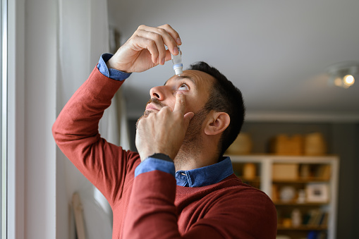 Close-up of young man applying eye drops to treat dry eye and irritation at home
