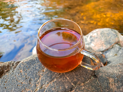 A glass cup of tea on stone by the river in a sunny day