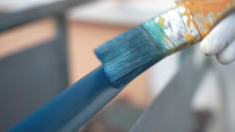 Close-up shot of renovated balcony frame painted with protective blue colour, repairman in gloves using paintbrush for coating metal surface with special chemical blue colour to prevent corrosion. Restoration of an aged weathered balcony frame, eroded st