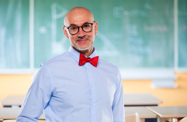 Portrait of mid aged professor standing in front of blackboard. Male teacher wearing glasses and bow tie.