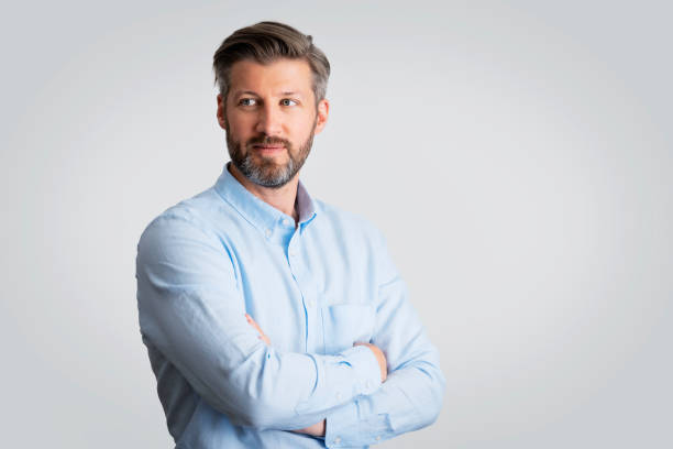 Studio portrait of mid aged businessman against isolated grey background Close-up of mid aged businessman studio portrait against isolated background. Confident man wearing shirt. Copy space. looking away stock pictures, royalty-free photos & images