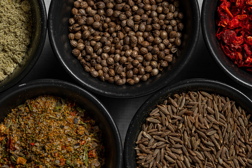 Assorted Georgian spices in bowls. saffron, Svan salt, suneli hops, cloves, raisins, allspice peas and others. Spices lie in black, round, ceramic bowls. The bowls stand on a light, linen tablecloth.