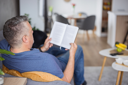 Man reading a book while sitting comfortably at sofa and enjoying weekend