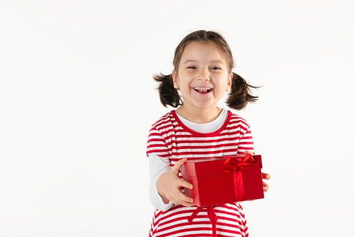 Caucasian girl is holding a red gift box in her hands and is looking at camera.