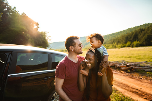 Adventurous married couple with little baby standing beside their car in nature on a sunny day