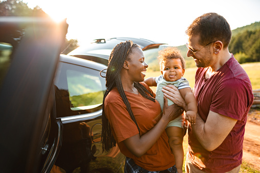 Adventurous married couple with little baby standing beside their car in nature on a sunny day