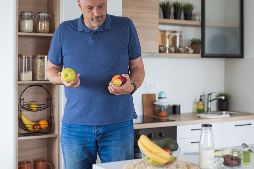 Man picking up fruit at the kitchen and making a snack