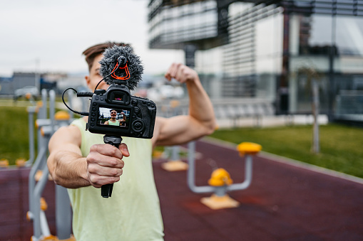 Young muscular man recording vlog about exercise in an outdoor gym.