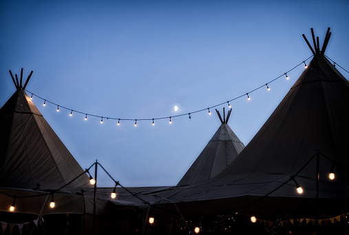 The moon shining behind wedding tipi's decked out with festoon lights.