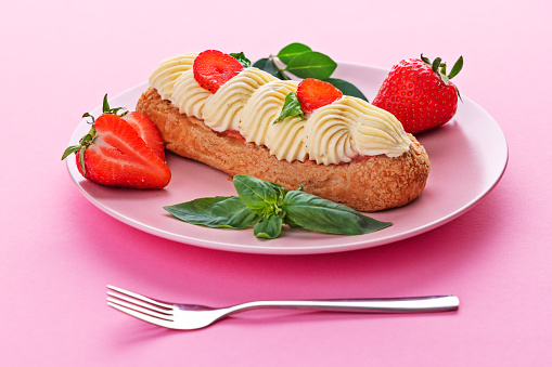French eclair grazed with chocolate and fruity strawberry cream or sweet Italian profiteroles and fresh juicy strawberries, food on pink background