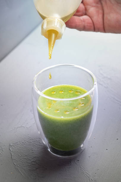 l'olio aromatizzato viene gocciolato da una bottiglia in un bicchiere di zuppa di spinaci verdi su uno sfondo grigio, cucina gourmet vegetariana sana, focus selezionato - salad green pouring dip foto e immagini stock