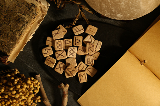 Wooden runes, dried flowers and old book on black table, flat lay