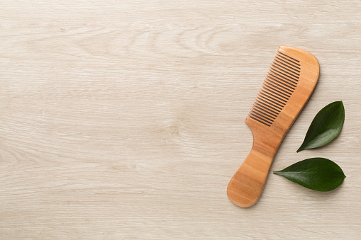Hair comb with green leaves wooden on background. Top view