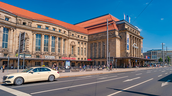 Leipzig, Germany - August 2, 2022: Modern taxi car. Cityscape of historical downtown and shopping center. Main train station in Leipzig at summer hot sunny day.
