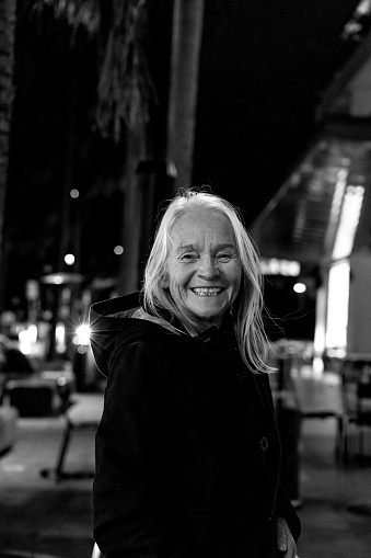 Black and white portrait of smiling senior woman in city at night, background with copy space, full frame vertical composition