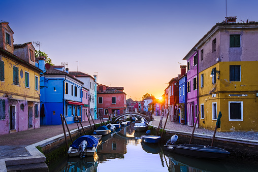 Sunrise in colorful fishing village Burano, Italy; boats and buildings reflect in calm water