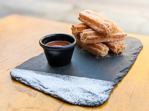 Traditional spanish churros with hot chocolate sauce on a rustic wooden table