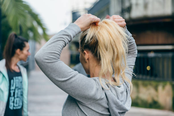 Blonde woman runner tying her hair in a ponytail before training Unrecognizable blonde woman runner tying her hair in a ponytail next to female friends before training woman tying hair in ponytail getting ready for exercising stock pictures, royalty-free photos & images