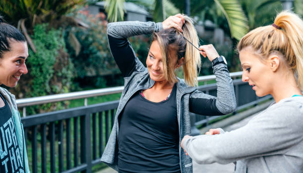 Blonde woman runner tying her hair in a ponytail before training Smiling blonde woman runner tying her hair in a ponytail next to female friends before training woman tying hair in ponytail getting ready for exercising stock pictures, royalty-free photos & images