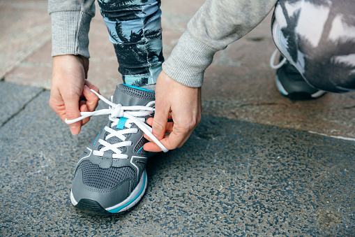 Close up of unrecognizable woman runner tying her sneakers laces to training on town