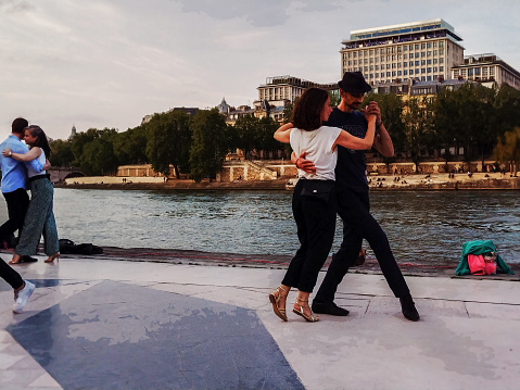 05-14-2023 Paris, France Tango in Paris : Tango on riverbank of Seine in fantastic May.  pairs dancing. Stylized in monochrome. Motor boat is sailing against the current