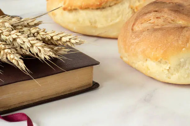 Two loaves of read, wheat, and closed holy bible book on the table. A close-up.