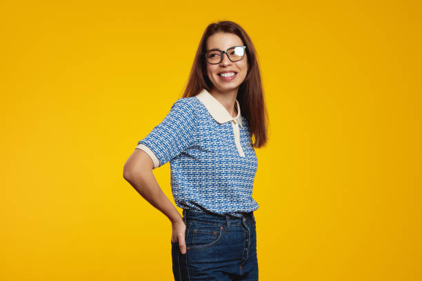 istock Young girl with eyeglasses smiling while looking at free empty space, holding hands in pockets 1500438115