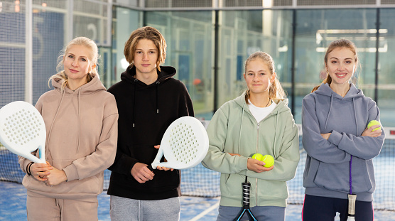 Group photo of four padel players, adult women and teenage boy and girl, standing in court.
