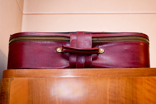 Leather travel suitcase placed on the antique old wooden wardrobe.