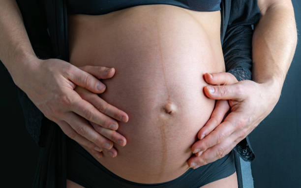 nahaufnahme des nackten runden bauches einer schwangeren mutter in unterwäsche, die von den händen der mutter und des vaters gehalten wird. letzter schwangerschaftsmonat - 36. woche. frontalansicht. schwarzer hintergrund. - two parent family naked men couple stock-fotos und bilder