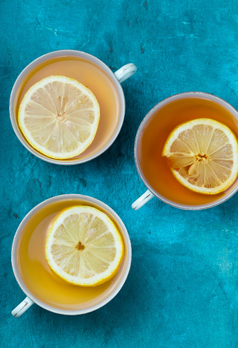 Fresh and colorful photo of three tea cups with slices of lemon inside. Super attractive contrast with a variety of tones and textures.