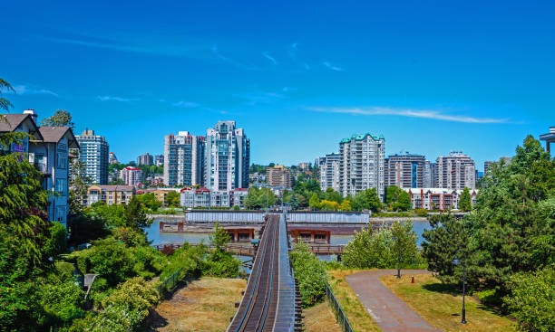 Railway Over River in New Westminster  City Railway over Fraser river on the waterfront in Downtown of New Westminster Fraser River, green trees at the promenade on a background of clear blue sky new westminster stock pictures, royalty-free photos & images