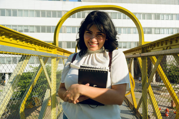 portrait of young venezuelan woman smiling hugging a book looking at the camera stock photo