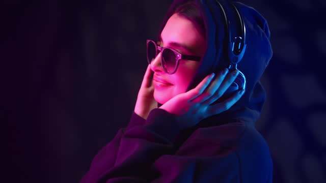 Fashion hipster woman listening music headphones dancing relaxing futuristic neon ultraviolet light