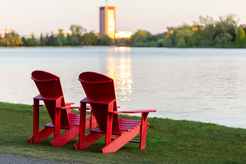 Adirondack red chairs by lake shore in Ottawa, Canada. Peacefull evening scene. Serene beauty.