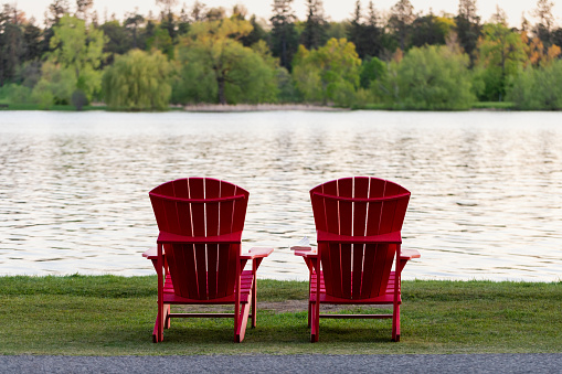 Adirondack red chairs by lake shore. Peacefull scene. Serene beauty. Relaxation concept.