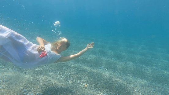 Young girl with long blond hair, dressed in a pink swimsuit eating a fresh apple on a sunny day at the beach with ocean view.