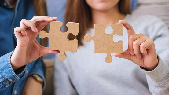 Closeup image of a couple women holding and putting a piece of wooden jigsaw puzzle together