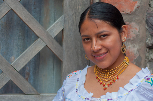 native latin america girl looking at camera and smiling wearing traditional dress of her culture and gold earrings and necklaces. High quality photo