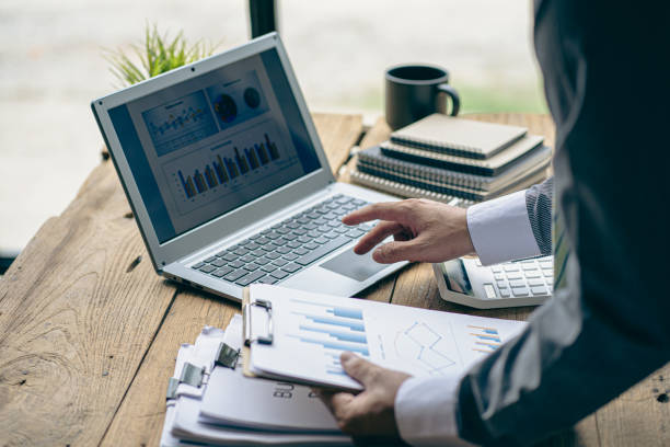 istock Businessman holding pen pointing at marketing graph and working on laptop computer working using calculator for math on wooden table at office business finance concept 1500475867